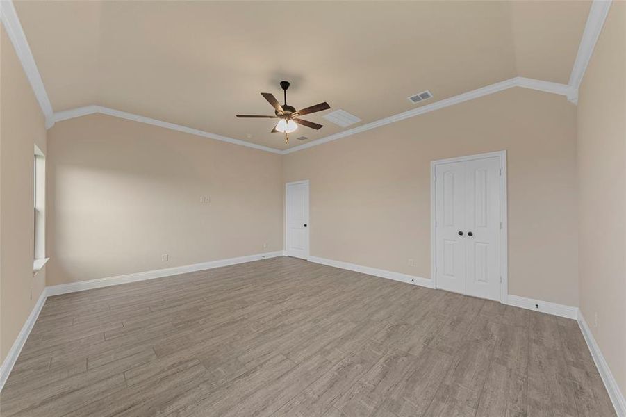 Unfurnished room featuring a ceiling fan, light wood finished floors, baseboards, vaulted ceiling, and crown molding