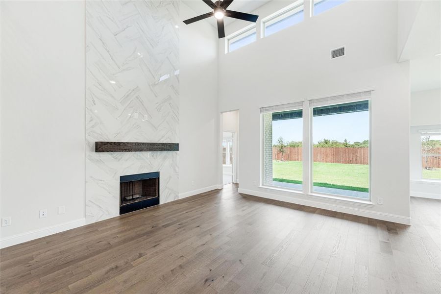 Open living room with two-story ceiling, herringbone tile fireplace, hardwood floors, and large windows overlooking backyard