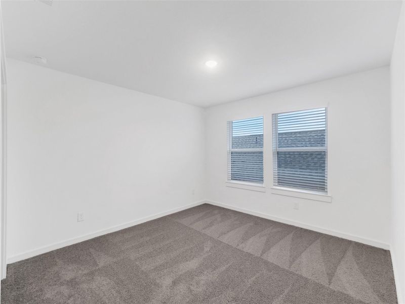Fourth bedroom with neutral walls and carpeting. It features two windows with blinds, allowing natural light to filter in, creating a clean and spacious feel.