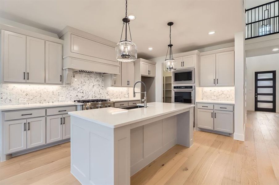 Kitchen featuring a kitchen island with sink, sink, light hardwood / wood-style flooring, decorative backsplash, and appliances with stainless steel finishes