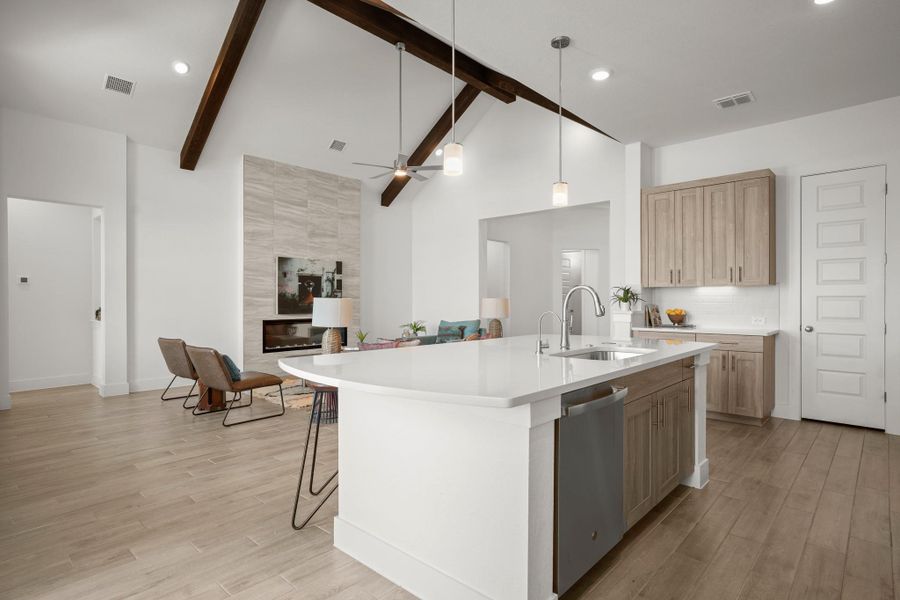 An open-concept living space highlights exposed wooden beams and a contemporary fireplace, connecting seamlessly to a kitchen island.