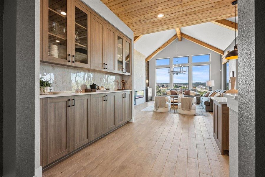 Bar area with a chandelier, light wood finished floors, wood finish cabinetry, glass insert cabinets, and tasteful backsplash