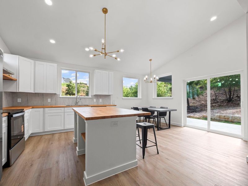 Modern kitchen and dining area featuring white cabinetry, light wood-finish countertops, stainless steel appliances, and wood-finish flooring