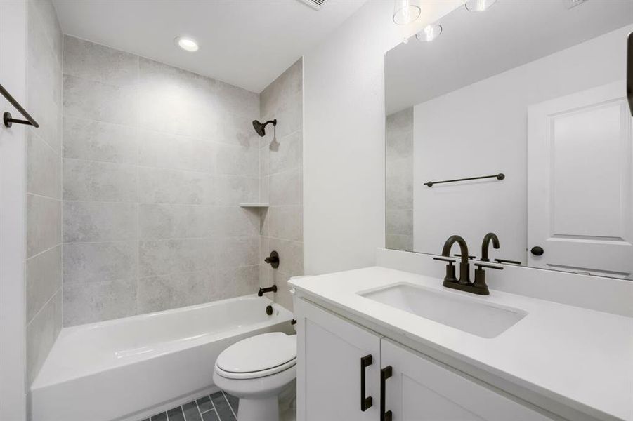 Bathroom featuring a white bathtub with light gray tile surround, dark bronze fixtures, white vanity with integrated sink, and a large mirror