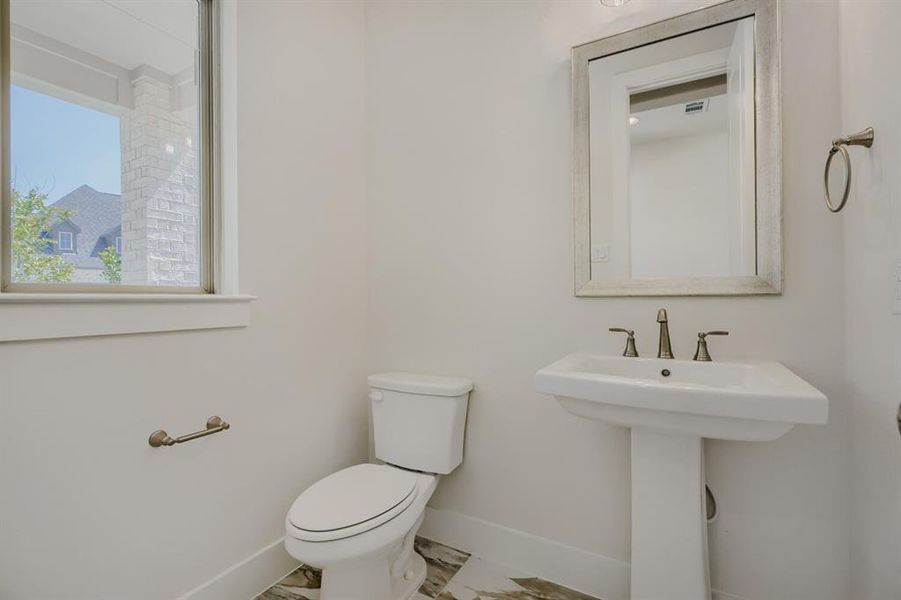 Bathroom with pedestal sink, framed mirror, and two-piece toilet