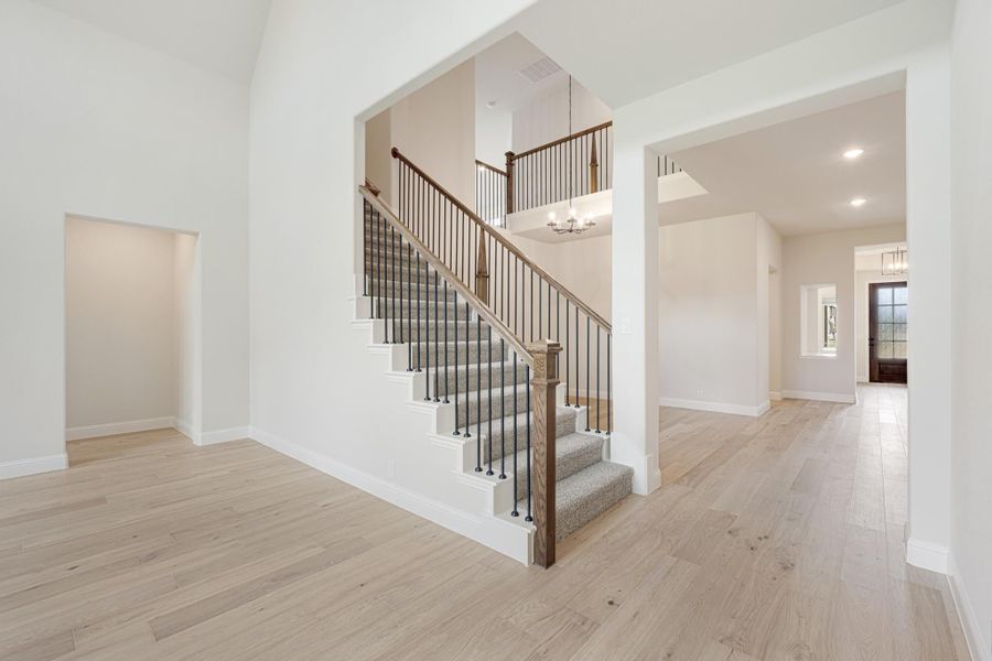 Two-story foyer with carpeted staircase, iron balusters, wood handrail, and light hardwood floors Two-story foyer with carpeted staircase, iron balusters, wood handrail, and light hardwood floors