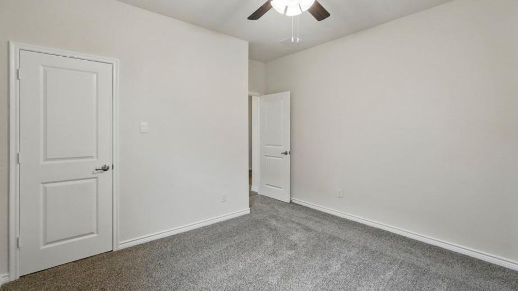 Carpeted interior space featuring light-toned walls, white trim, and a ceiling fan with integrated lighting