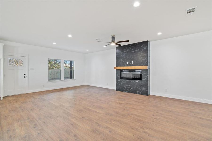 Unfurnished living room featuring ceiling fan, a high end fireplace, and light wood-type flooring