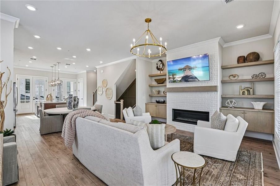 Living area featuring a chandelier, crown molding, a linear fireplace with cabinetry, recessed lighting, and hard surface flooring
