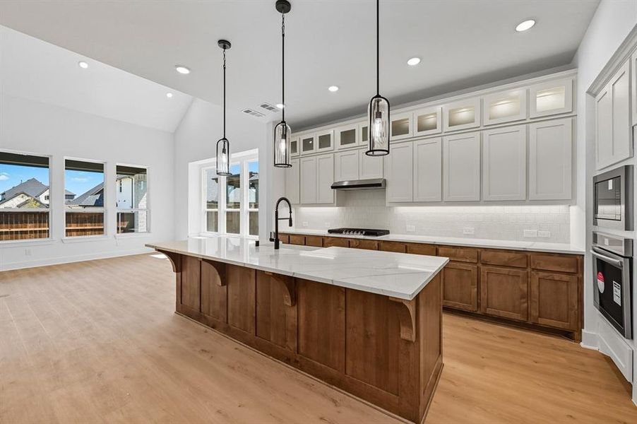 Kitchen featuring brown cabinets, a kitchen breakfast bar, tasteful backsplash, glass insert cabinets, and an island with sink Kitchen featuring brown cabinets, a kitchen breakfast bar, tasteful backsplash, glass insert cabinets, and an island with sink