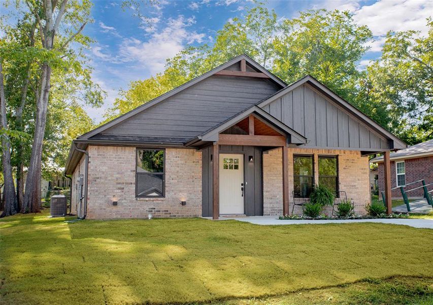 View of front of property featuring a front yard, brick siding, and board and batten siding View of front of property featuring a front yard, brick siding, and board and batten siding