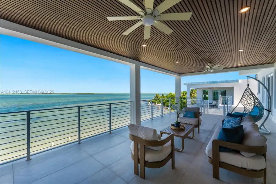 Covered terrace featuring a slatted wood ceiling, recessed lighting, ceiling fans, large-format tile flooring, and a stainless steel cable railing system Covered terrace featuring a slatted wood ceiling, recessed lighting, ceiling fans, large-format tile flooring, and a stainless steel cable railing system
