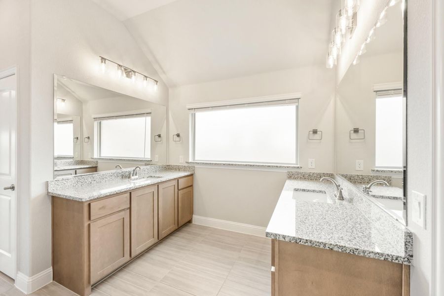Bathroom with dual vanities, granite countertops, wood cabinets, and vaulted ceiling