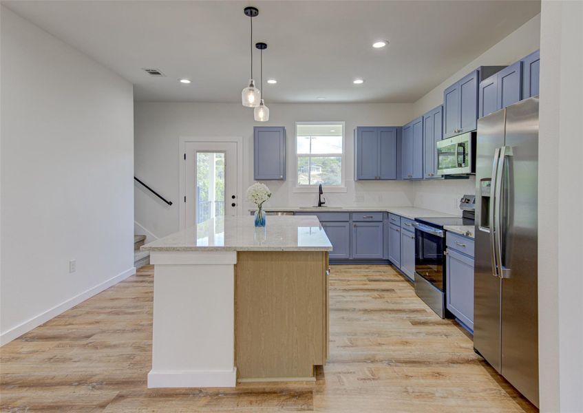 Kitchen with appliances with stainless steel finishes, pendant lighting, light wood-type flooring, a kitchen island, and recessed lighting