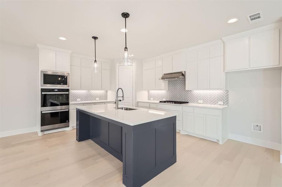 Kitchen with exhaust hood, light hardwood / wood-style flooring, a center island with sink, sink, and white cabinetry