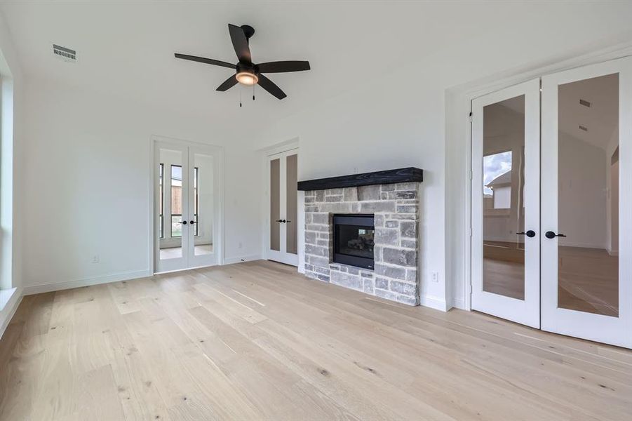 Unfurnished living room featuring french doors, light hardwood / wood-style flooring, a stone fireplace, and ceiling fan