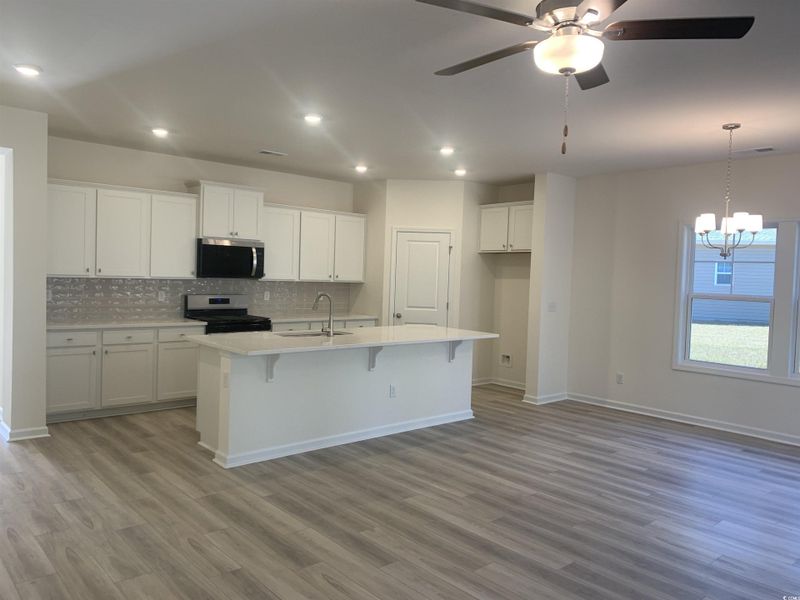 Kitchen featuring white cabinetry, stainless steel appliances, a kitchen bar, a kitchen island with sink, and light wood-type flooring