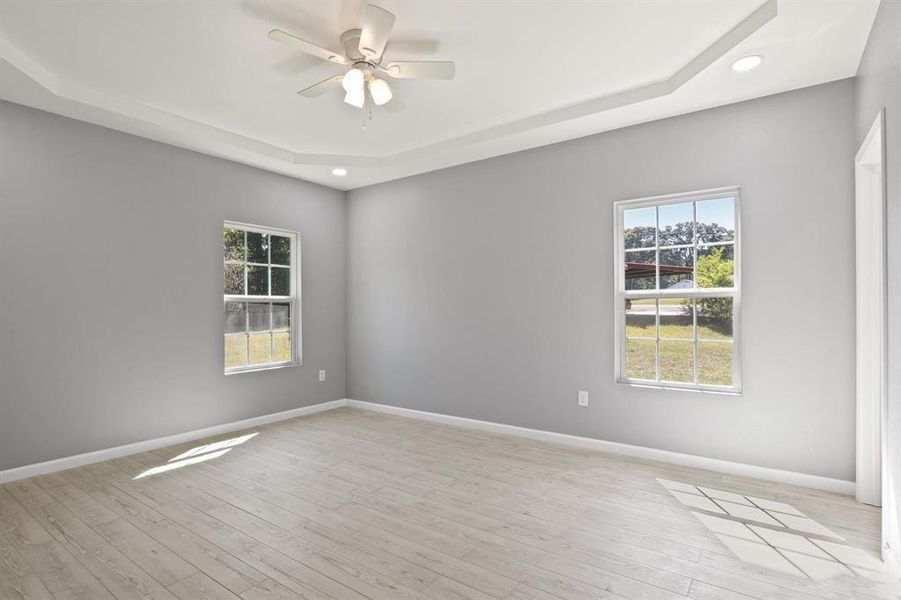 Spare room with a raised ceiling, light wood-style floors, healthy amount of natural light, and recessed lighting
