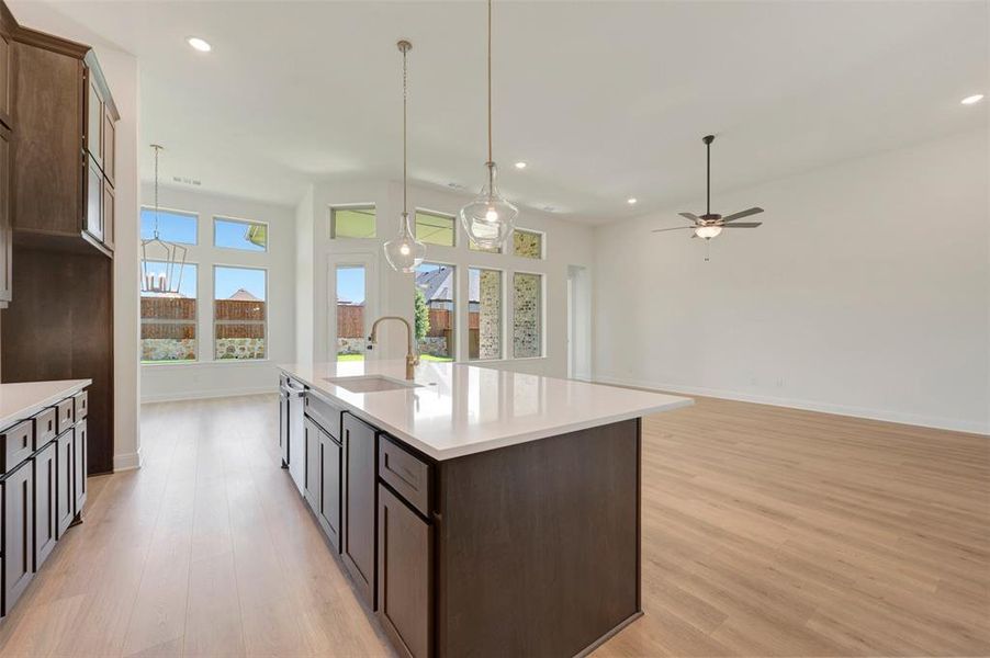 Open-concept kitchen and living area featuring a large center island with a sink, pendant lighting, wood-finish flooring, recessed lighting, and a ceiling fan Open-concept kitchen and living area featuring a large center island with a sink, pendant lighting, wood-finish flooring, recessed lighting, and a ceiling fan