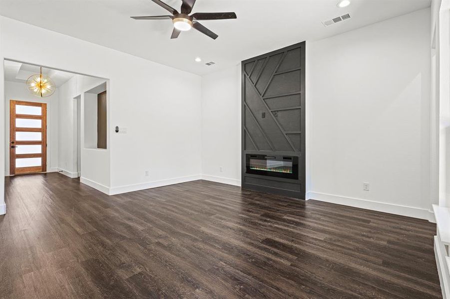 Unfurnished living room with a large fireplace, visible vents, baseboards, and dark wood-style flooring