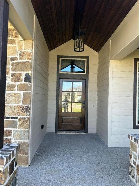 Covered entryway featuring a wood-paneled ceiling, stone column accents, and a wood-frame door with glass panels