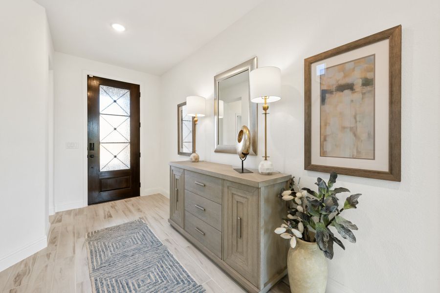 Entryway with dark wood glass-panel front door, gray console cabinet, wall mirror, and light wood floors