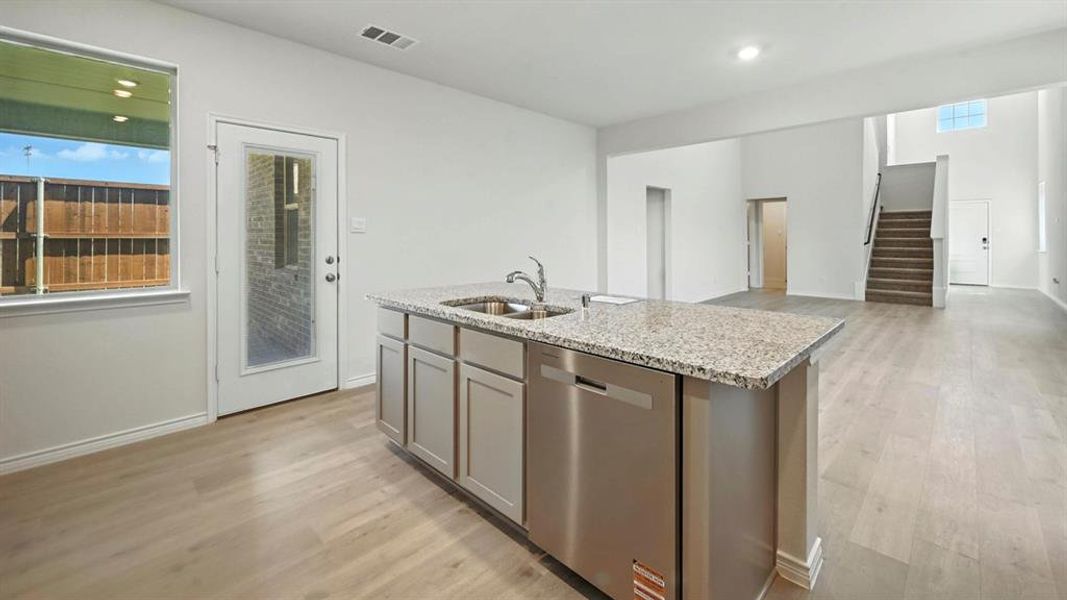 Kitchen featuring stainless steel dishwasher, light stone counters, light wood finished floors, a center island with sink, and open floor plan Kitchen featuring stainless steel dishwasher, light stone counters, light wood finished floors, a center island with sink, and open floor plan