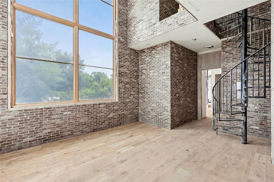Interior space featuring a tall window with light wood framing, exposed brick walls, light wood-finish flooring, and a black metal spiral staircase
