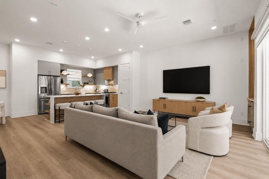 The kitchen and living room unfold as a cohesive composition, where intentional spacing, elevated ceilings, and balanced proportions create a sense of openness. At its center, the kitchen anchors the home while the surrounding spaces adapt seamlessly to both daily routines and social gatherings.