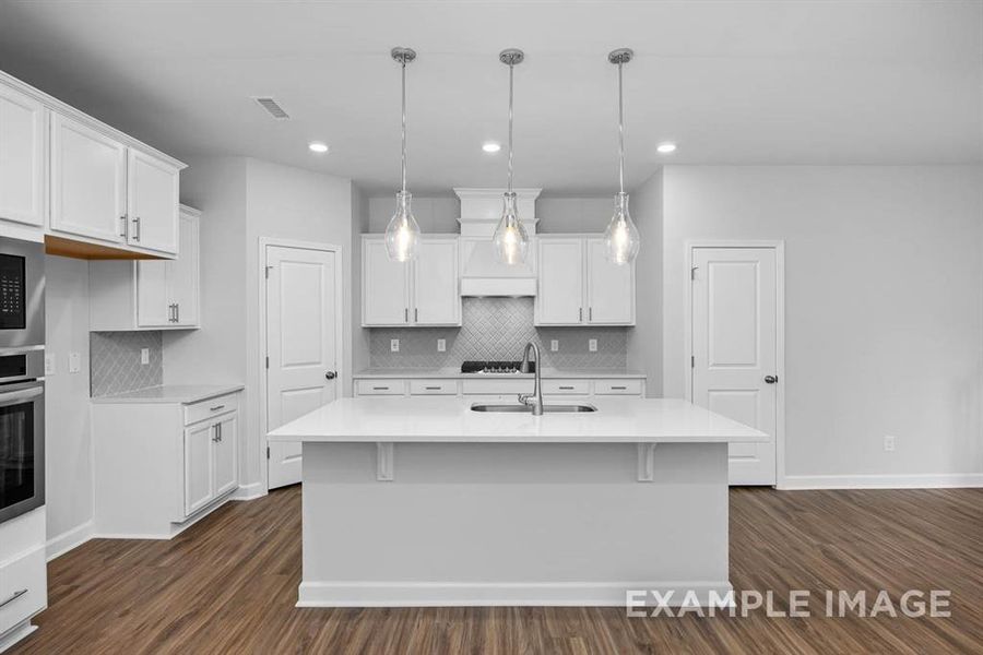 Kitchen with pendant lighting, a center island with sink, white cabinets, and dark wood-type flooring