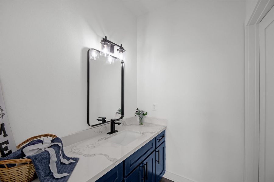 Bathroom features a sleek, modern design with a white countertop, navy blue cabinetry, and a stylish black-framed mirror with elegant lighting. Bathroom features a sleek, modern design with a white countertop, navy blue cabinetry, and a stylish black-framed mirror with elegant lighting.