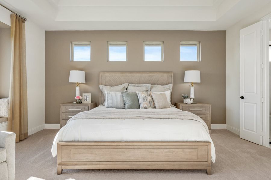 Master bedroom with king bed, wood nightstands, and four small windows above a tan accent wall