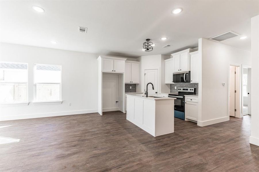 Kitchen with sink, white cabinetry, electric stove, a kitchen island with sink, and decorative backsplash