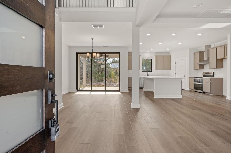 Luxurious open concept floor plan featuring wood-look tile planks, oversized glass sliders, and a grand staircase