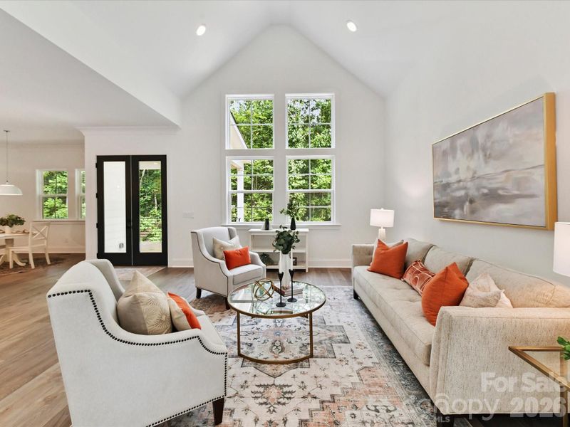 Spacious living room with vaulted ceilings, abundant natural light from large windows, and direct access to the deck overlooking the wooded lakefront setting.