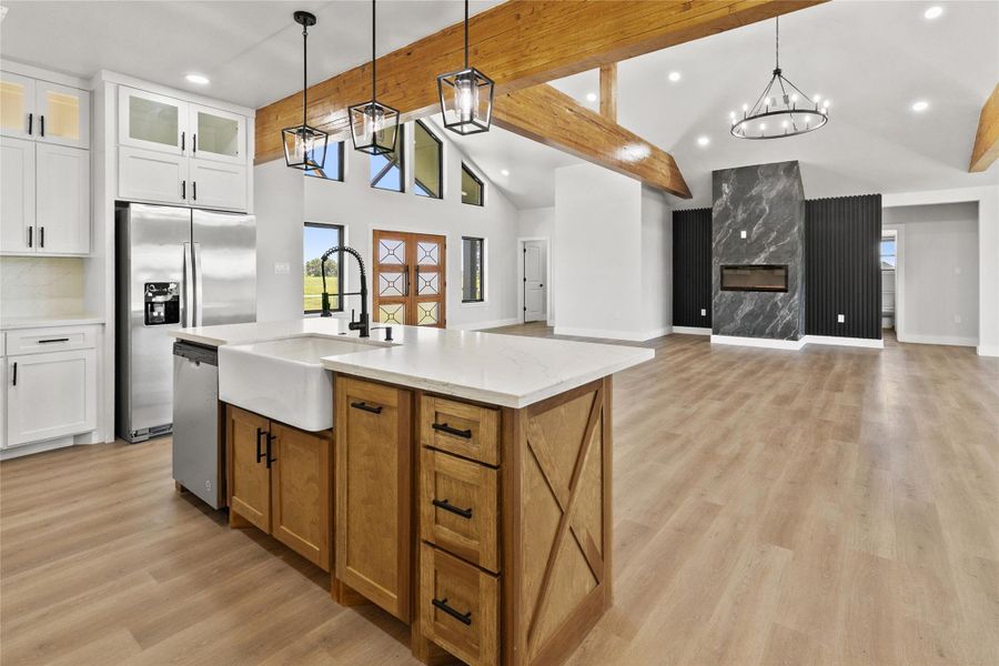 The kitchen blends style and function with quartz countertops, a wood island with an apron-front farmhouse sink, beverage refrigerator, wine storage, under-counter microwave, lighted glass-front cabinetry, and a large walk-in pantry.