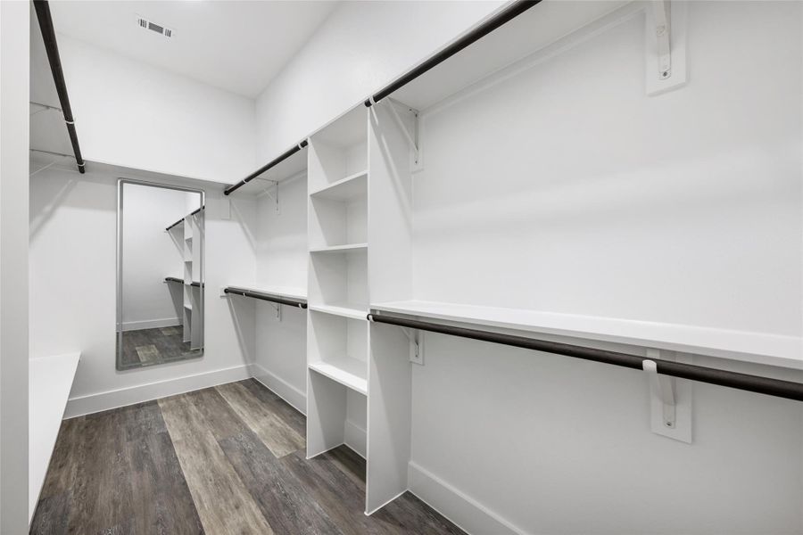 Walk-in closet featuring wood-finish flooring, built-in shelving, black hanging rods, and a full-length wall mirror