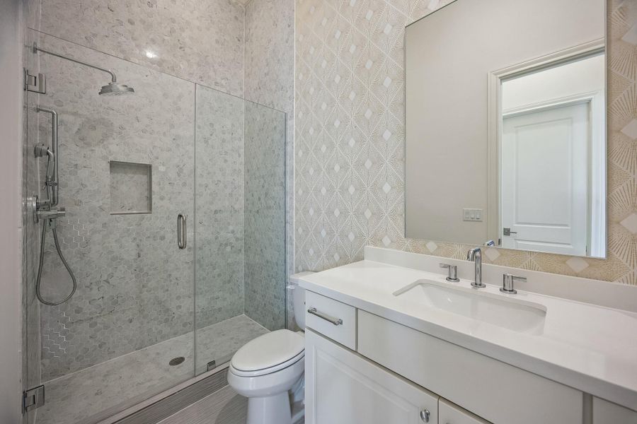 The stylish second-floor bath features a walk-in shower, neutral finishes, and playful wallpaper for a touch of personality.
