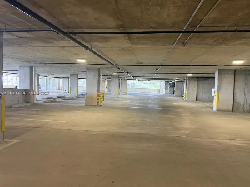 Covered parking garage featuring reinforced concrete structural columns, overhead flush-mount lighting, and concrete flooring
