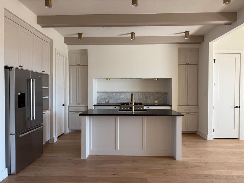 Kitchen with sink, a center island with sink, high end refrigerator, and beamed ceiling