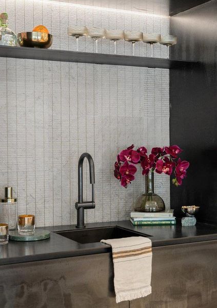 Integrated wet bar featuring a matte black sink and faucet, textured tile backsplash, dark wood-finish cabinetry, and under-cabinet lighting