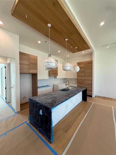 Kitchen with modern cabinets, hanging light fixtures, a center island with sink, brown cabinets, and recessed lighting