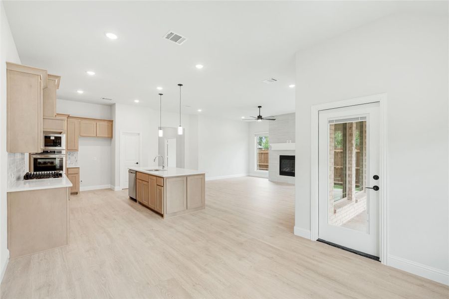 Open-concept kitchen and living area with light wood cabinets, center island, and fireplace visible in background