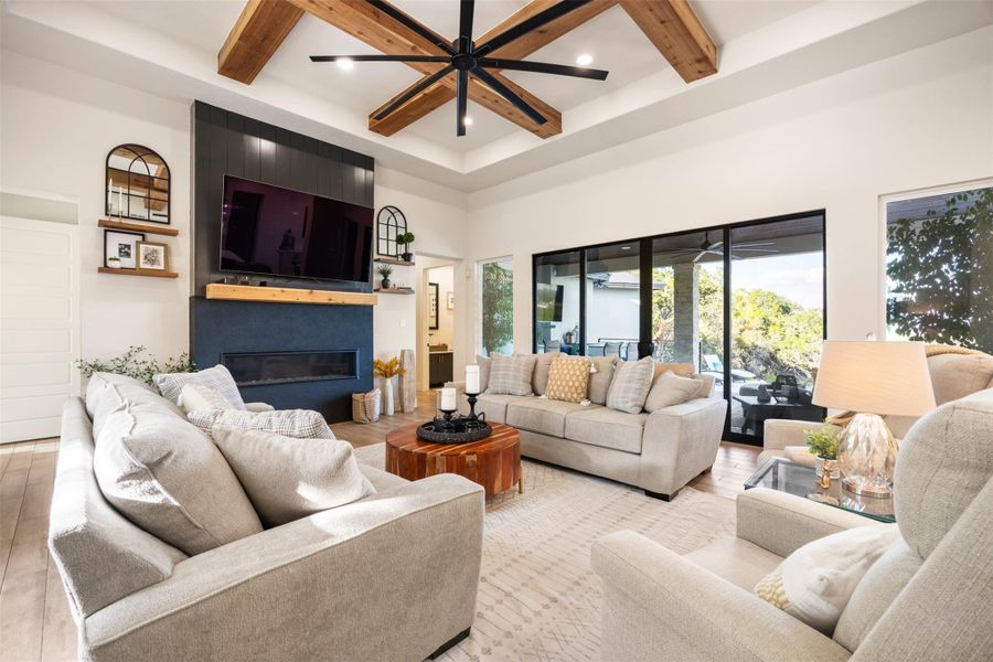 Living room featuring a towering ceiling, beamed ceiling, a large fireplace, ceiling fan, and light hardwood / wood-style floors Living room featuring a towering ceiling, beamed ceiling, a large fireplace, ceiling fan, and light hardwood / wood-style floors