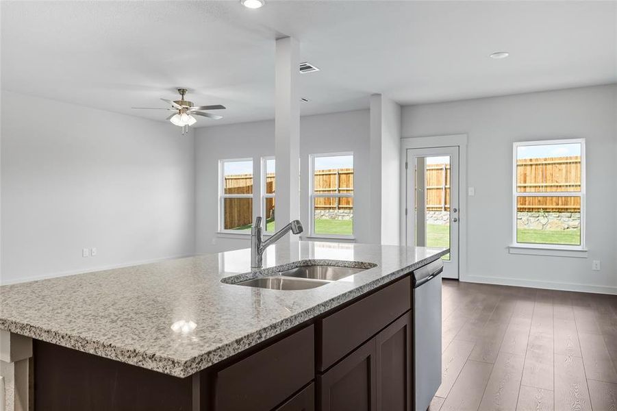 Kitchen with dark brown cabinetry, a kitchen island with sink, dark wood-type flooring, light stone countertops, and recessed lighting Kitchen with dark brown cabinetry, a kitchen island with sink, dark wood-type flooring, light stone countertops, and recessed lighting