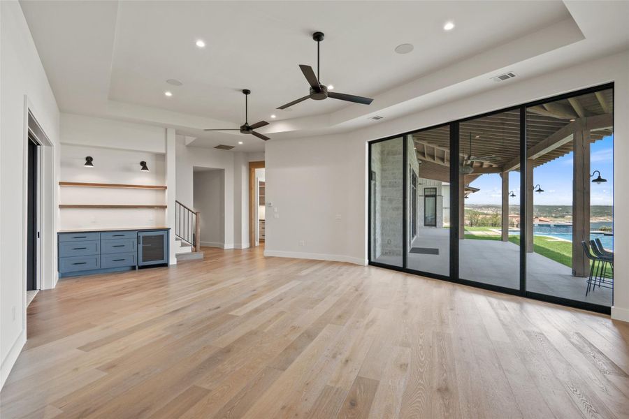 Unfurnished living room with a tray ceiling, stairs, light wood-style floors, ceiling fan, and recessed lighting