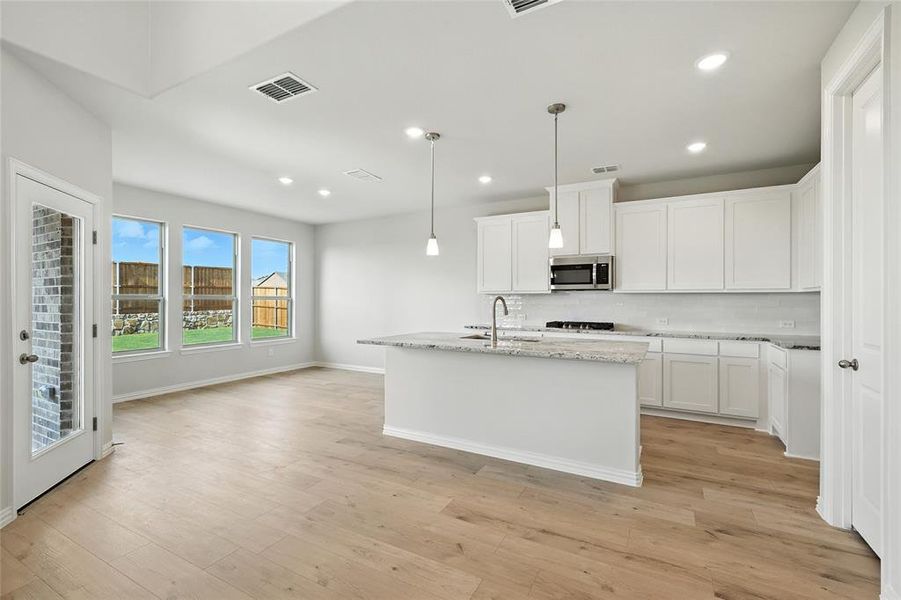 Kitchen with tasteful backsplash, a center island with sink, white cabinetry, recessed lighting, and hanging light fixtures Kitchen with tasteful backsplash, a center island with sink, white cabinetry, recessed lighting, and hanging light fixtures