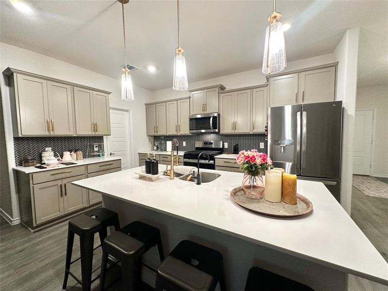 Kitchen with a kitchen breakfast bar, appliances with stainless steel finishes, decorative backsplash, gray cabinetry, and pendant lighting Kitchen with a kitchen breakfast bar, appliances with stainless steel finishes, decorative backsplash, gray cabinetry, and pendant lighting