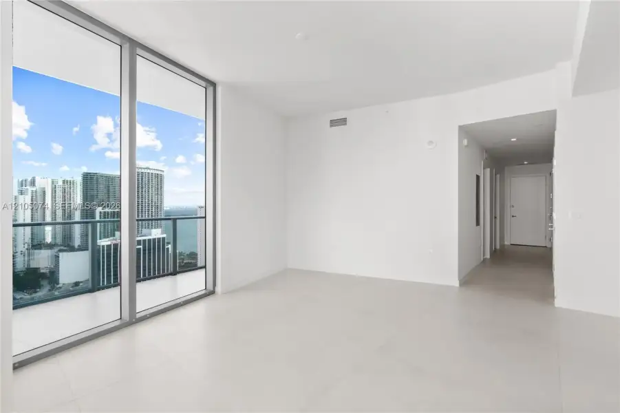 Floor-to-ceiling glass panel walls, light-toned tile flooring, recessed ceiling lighting, and a private balcony with metallic railing