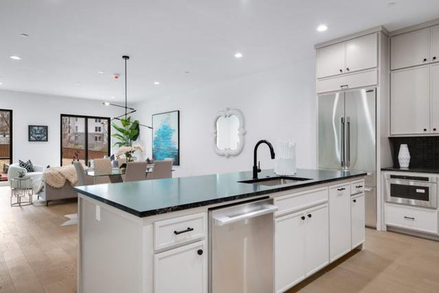 Kitchen featuring a kitchen island with sink, a sink, stainless steel appliances, and dark countertops